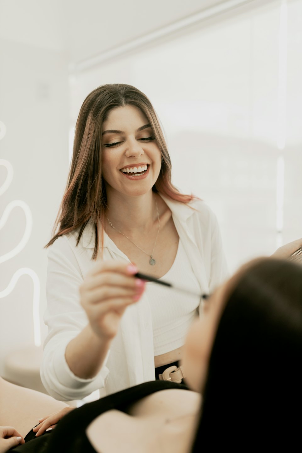 Kosmetikerin trägt Mascara bei einer Kundin im Salon auf.