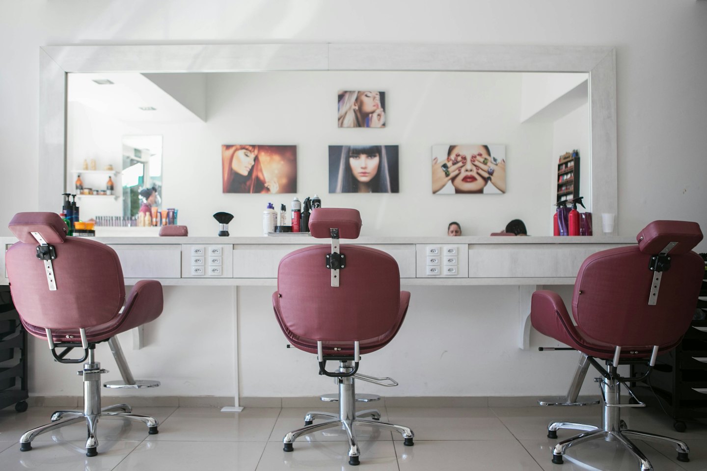 Moderne Friseurstühle an einer weißen Theke mit Schönheitsprodukten.