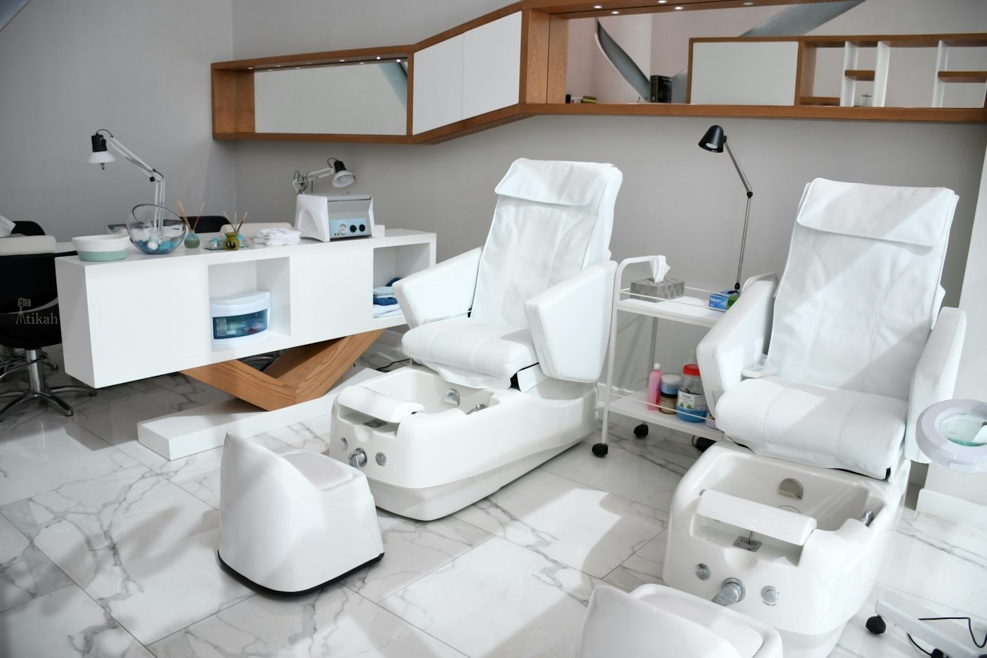 Zwei weiße Spa-Pediküre-Stühle mit Fußbädern in einem modernen Salon.